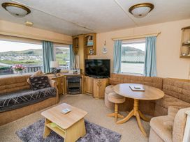 A living room with sofas a round wooden table a small wooden coffee table a television and windows with blue curtains at GM18 Clarach Bay near Aberystwyth