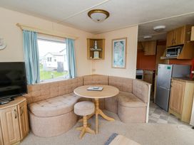A living area with a corner sofa a round table a stool a television and a kitchen with wooden cabinets at GM18 Clarach Bay near Aberystwyth