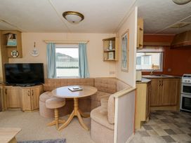 A living area with a round wooden table and curved sofa next to a television and an open kitchen at GM18 in Clarach Bay near Aberystwyth