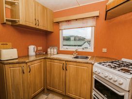 A kitchen with wooden cabinets a toaster a kettle a sink a gas stove and a window showing outside at GM18 in Clarach Bay near Aberystwyth