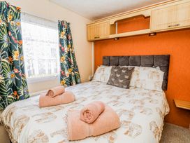 A bedroom with a bed with patterned bedding and folded towels near a window with floral curtains at GM18 in Clarach Bay near Aberystwyth