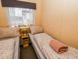 A small bedroom with two single beds a bedside table with a lamp and a window with lace curtains at GM18 Clarach Bay near Aberystwyth