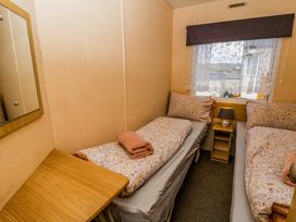 A small bedroom with two single beds bedside table lamp and a window with blinds at GM18 Clarach Bay near Aberystwyth