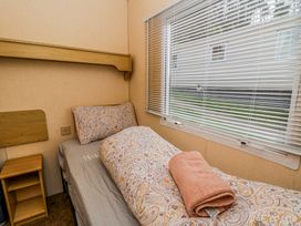 A small bedroom with a single bed a patterned duvet and pillow a folded towel a wooden side table and blinds on the window at GM18 Clarach Bay near Aberystwyth