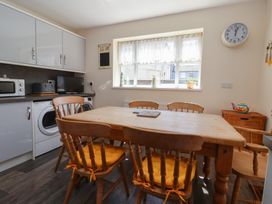 A dining area with a wooden table and six wooden chairs with yellow cushions a washing machine microwave and toaster on the counter and a window with lace curtains at 4 Queen Street in Withernsea