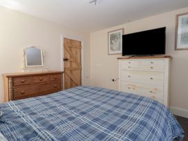 A bedroom with a bed covered in blue plaid bedding a wooden door a wooden dresser with a mirror and a white dresser with a television at 4 Queen Street Withernsea