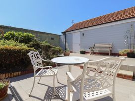 An outdoor patio area with white metal chairs and a round table with a stone top next to a white wooden building with a bench and potted plants at 4 Queen Street in Withernsea