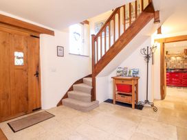 A hallway with wooden staircase and door a small table with baskets and a coat stand at Church Thatch in Abbotskerswell