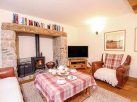A living room with a stone fireplace a wood burning stove a television and a coffee table with tea and cake at Church Thatch in Abbotskerswell