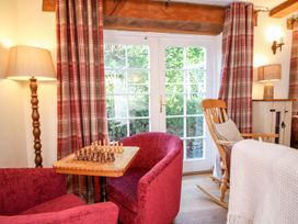 A seating area with two red armchairs and a wooden chess table by glass doors with red plaid curtains at Church Thatch in Abbotskerswell