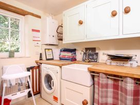 A laundry room with a washing machine sink white cabinets wooden countertop and a high chair at Church Thatch in Abbotskerswell