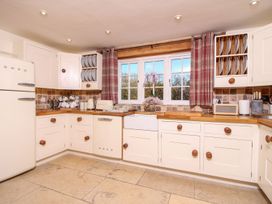 A kitchen with cream cabinets wooden countertops a farmhouse sink and a window with red plaid curtains at Church Thatch in Abbotskerswell