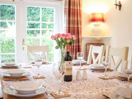 A dining table set with plates glasses a bottle of wine and a vase of pink flowers by a window at Church Thatch in Abbotskerswell