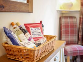 A wicker basket with wine bottles and snacks on a wooden table next to a plaid chair at Church Thatch in Abbotskerswell