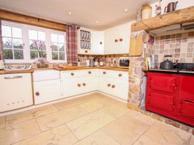 A kitchen with white cabinets a red stove wooden countertops and a window with curtains at Church Thatch in Abbotskerswell