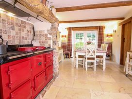 A kitchen with a red stove and a dining table with six white chairs near a window with plaid curtains at Church Thatch in Abbotskerswell