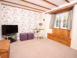 A living room with a television two purple ottomans a small desk and window seating at Church Thatch in Abbotskerswell