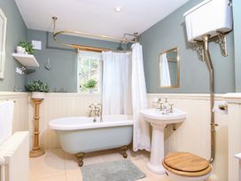 A bathroom with a clawfoot bathtub shower curtain pedestal sink and high level toilet at Church Thatch in Abbotskerswell