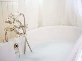 A white bathtub with a silver faucet and handheld shower head filled with water and bubbles at Church Thatch in Abbotskerswell