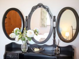 A black dressing table with three oval mirrors a vase of white flowers a heart shaped soap and a reed diffuser at Church Thatch in Abbotskerswell