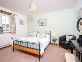 A bedroom with a double bed armchair bedside table and desk at Church Thatch in Abbotskerswell