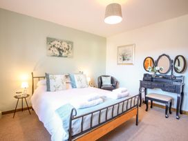 A bedroom with a double bed pillows and towels bedside tables a black dressing table with mirrors and a round chair at Church Thatch in Abbotskerswell