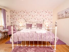 A bedroom with a metal bed frame, floral wallpaper, purple cushions, and purple rugs at Church Thatch in Abbotskerswell