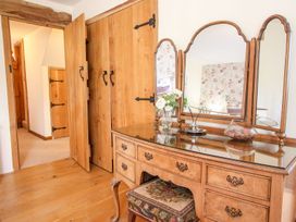 A wooden dressing table with a three-paneled mirror a vase with flowers and an upholstered stool in a room at Church Thatch in Abbotskerswell