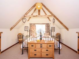 A bedroom with a wooden dresser bed floral pillows and curtains and wooden beams on the ceiling at Church Thatch in Abbotskerswell