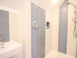 A bathroom shower area with striped wall tiles a showerhead and a small sink at Church Thatch in Abbotskerswell
