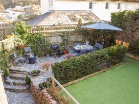 A garden patio with a dining table set under an umbrella surrounded by chairs and a barbecue grill at Church Thatch in Abbotskerswell
