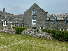 A stone house with multiple windows and a grassy area at Mallow Cottage in Langton Matravers