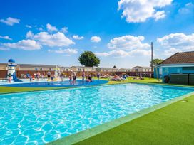 An outdoor pool area with a fountain and sun loungers at Dune Delight - Hayling Island
