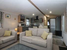 A living room with a sofa and kitchen area at Woodland Way in Benllech
