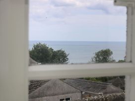 A view of the sea and trees through a window at Driftwood Cottage in St. Austell