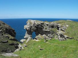 A rocky coastal landscape with a person walking near a rock formation at Tremorla in Boscastle