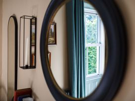 A mirror reflecting a window with curtains and framed pictures at Grove House in Grange-Over-Sands