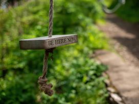 A wooden sign hanging from a rope with text in a garden at The Pink House Nine Wells near Solva