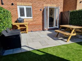 A garden with a patio, barbecue grill, and wooden furniture at Hafan Rhos Rhos-On-Sea