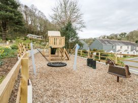 A playground with a playhouse, swing, and seesaw at Trouts Reach Goldenbank near Budock Water