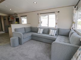A living room with a sectional sofa and windows at Puffin Way Holiday Caravan