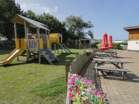 An outdoor play area with a playground and picnic tables at Puffin Way Holiday Caravan 