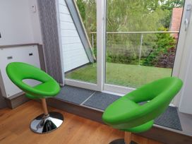 A living room with green chairs and a glass door leading to a balcony at Silver Copse in Frilford Heath Near Abingdon