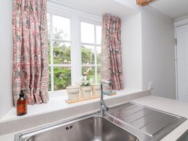 A kitchen window with curtains and a sink at Magdalen Cottage in Hook Norton