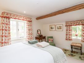 A bedroom with a bed and a chair at Magdalen Cottage in Hook Norton
