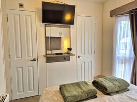A bedroom with a television and towels on a bed at Fernwood Lodge in Fritton near Belton, Norfolk