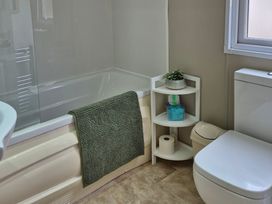 A bathroom featuring a bathtub, toilet, and shelf with toiletries at Fernwood Lodge in Fritton near Belton, Norfolk