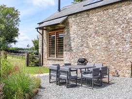 An outdoor area with a table and chairs near a stone wall at Lower Walreddon Barn Tavistock