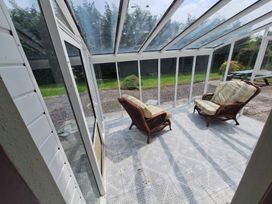 A conservatory with rattan chairs and a garden view at Lilly's Bungalow in Timoleague