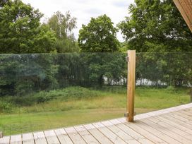 A wooden deck with a glass railing overlooking a grassy area and trees at Lakeside Lodge near Burwash